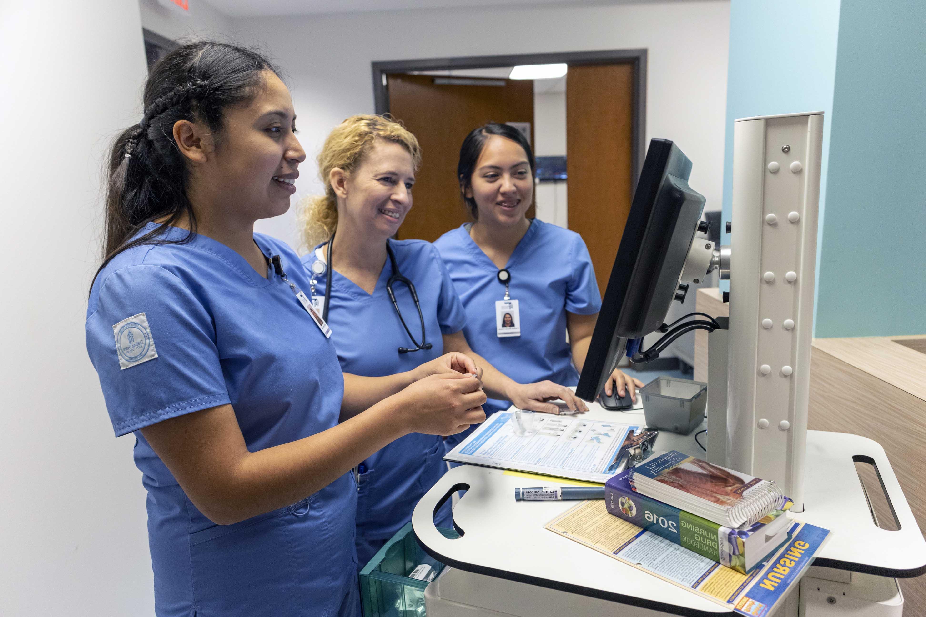 Health profession students in uniform looking at cart monitor